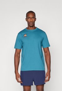 Teal sport t-shirt met korte mouwen, ronde hals en een oranje logo op de linkerborst. Gemaakt van ademend materiaal, nauwsluitend ontwerp.