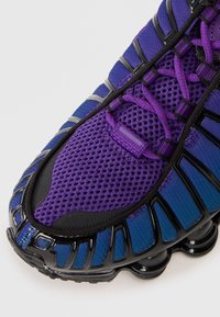 Purple and blue athletic shoe featuring a mesh upper, textured pattern, black accents, and a rounded sole with visible air cushioning.
