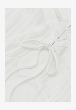 Közeli fehér szövet látványa finom függőleges csíkokkal, megkötött csipkés masnival, amely átfűzött a szemeken, és dekoratív varrási részletekkel.