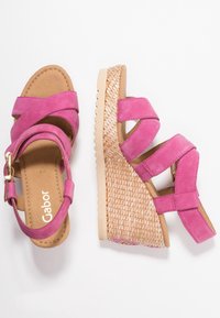 Sandali con zeppa in suede rosa con cinturini incrociati, dotati di un tacco intrecciato testurizzato e una suola in gomma. Chiusura con fibbia regolabile per una vestibilità perfetta.