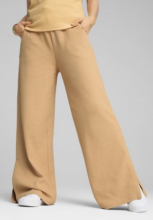 Pantalons larges beiges en tissu texturé, avec un logo subtil sur le côté, assortis à des baskets blanches.