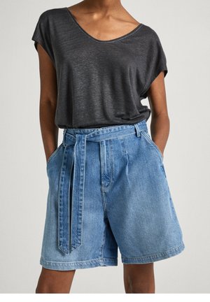 Kvinde iført en løs mørkegrå top med korte ærmer, stoppet ned i højtaljede lyseblå denimshorts med et matchende bælte.