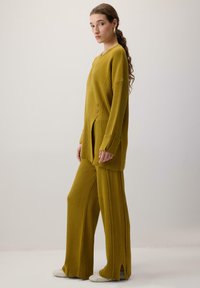 Sinine ribatud kudumine koosnev komplekt, mis sisaldab pikka tunikat külgsuundade ja nööpidega, koos laiade pükstega, mõlemad on valmistatud pehmest kangast.