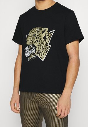 Black cotton t-shirt featuring a gold and black leopard graphic on a lightning bolt shape, with text "THE NOODLES" at the bottom.