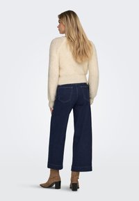 Cream fluffy sweater paired with dark blue wide-leg jeans. The jeans feature classic stitching and back pockets, worn with brown heeled boots.