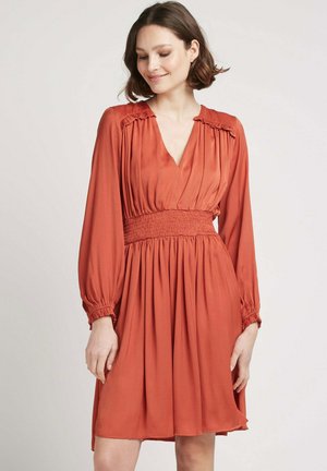 Robe couleur rouille, longueur genou, avec de longues manches froncées, un décolleté en V et une taille smockée, fabriquée dans un tissu doux et fluide.