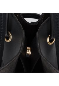 Gros plan de l'intérieur d'un sac à main en cuir noir montrant un fermoir magnétique doré et des œillets dorés fixant les poignées.