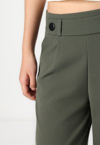 Olijfgroene op maat gemaakte broek met een gladde textuur, een zwarte knoopsluiting en een recht model met zijzakken.