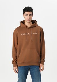 Bruine hoodie van katoen met een voorkeurszak, een capuchon met trekkoord en "TOMMY JEANS" branding op de borst in het wit.