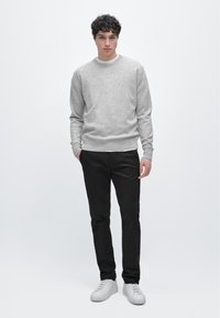 Jasnoszary sweter z okrągłym dekoltem, z prążkowanymi mankietami, w połączeniu z czarnymi spodniami i białymi trampkami. Prosty design, bez widocznych wzorów czy logo.