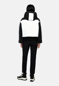 Gekürzte schwarz-weiße Jacke mit Kapuze, im Color-Block-Design, kombiniert mit schwarzen Hose und robusten schwarzen Stiefeln.