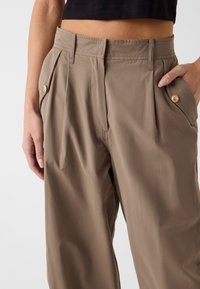 Lichte, beige broek met geplooide voorkant, zijzakken en gouden knoopaccenten. Soepele textuur en een casual pasvorm.