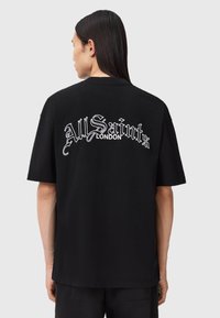 Sort bomulds-T-shirt med rund hals og afslappet pasform. Har hvidt scriptlogo "All Saints London" broderet på ryggen.