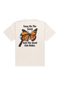 Camiseta de algodón color crema con un gran gráfico de mariposa negra y naranja y el texto: "Concéntrate en lo bueno, y lo bueno será aún mejor."
