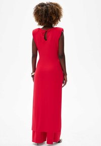 Rode mouwloze maxi-jurk met een getailleerde pasvorm, sleufopening aan de achterkant en een delicate strikdetail. Gladde textuur, ondervoering tot op de knie.