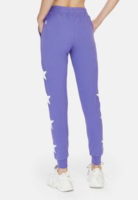 Paarse joggingsbroek van zacht katoen met witte sterpatronen langs de buitenbenen en elastische boorden. Inclusief zakken.