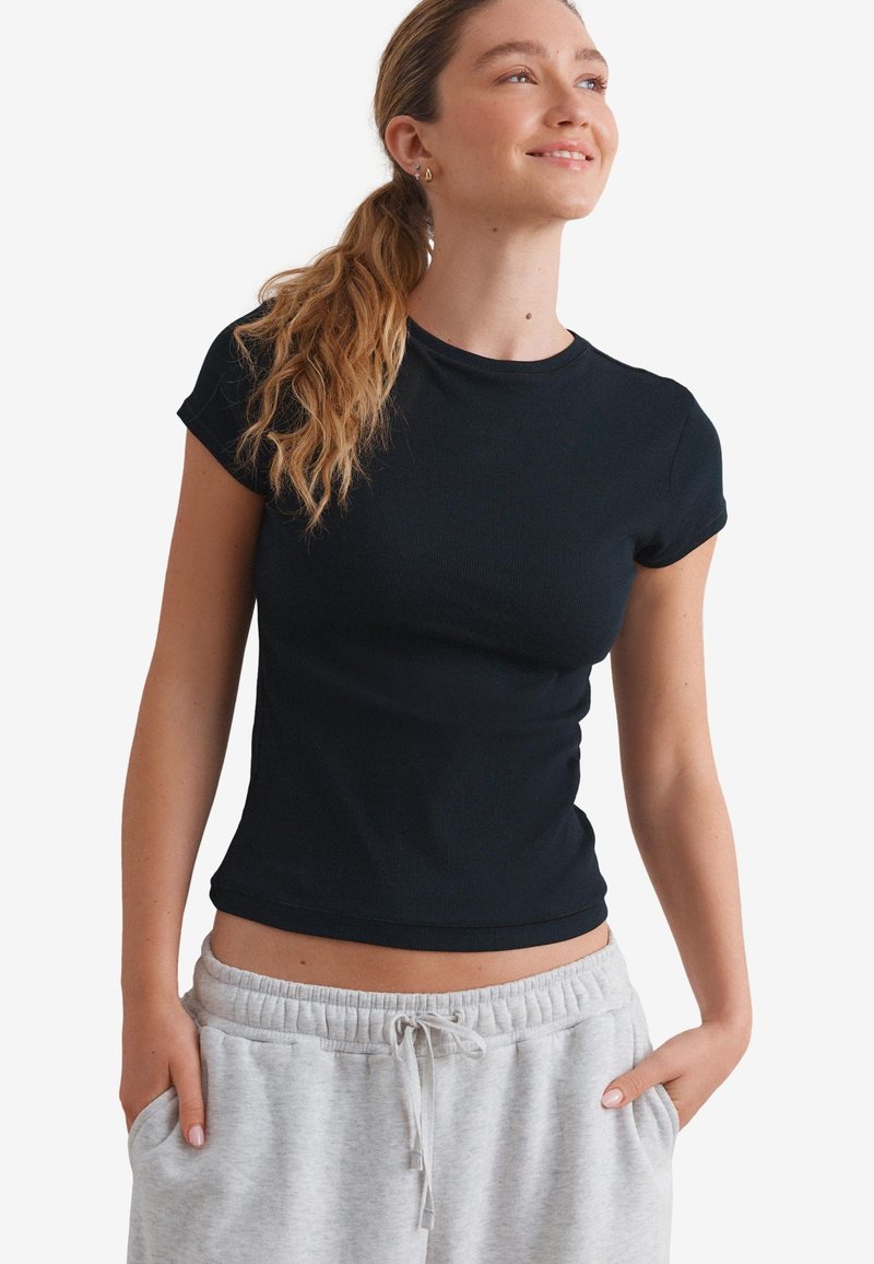 Black fitted t-shirt with short sleeves and a crew neckline. Smooth texture, paired with light gray sweatpants featuring an elastic waistband.