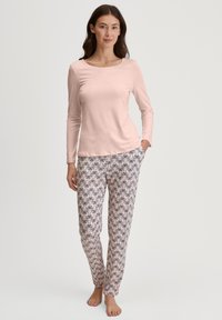 Lichtroze langwerpige top gecombineerd met een patroon broek met pastel bloemenontwerpen. Zachte, lichte stof; slim fit voor beide stukken.