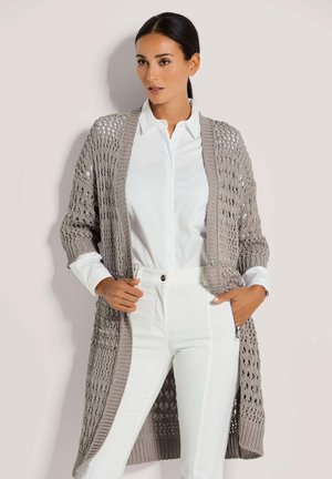 Lange, opengebreide cardigan in lichtgrijs, met een gestructureerd weefsel, ribgebreide manchetten en een ontspannen pasvorm. Gecombineerd met een witte blouse en broek.