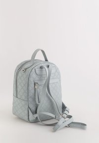 Mochila azul claro con un patrón hexagonal texturizado, forma curva, correas ajustables y cierre de cremallera. Presenta un pequeño bolsillo frontal.