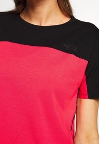 Koszulka z krótkim rękawem o żywym różowym kolorze korpusu i czarnych ramionach. Gładka faktura z subtelnymi detalami szwów oraz logo na piersi.