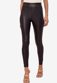 Leggings neri in faux pelle con vita alta, texture liscia e design aderente, abbinati a sandali beige con tacco a blocco.