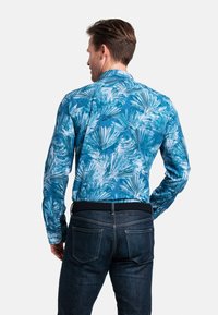 Langarmshirt met een blauw tropisch bladenpatroon, voorzien van een opstaande kraag en een getailleerde pasvorm, gecombineerd met een donkere spijkerbroek.