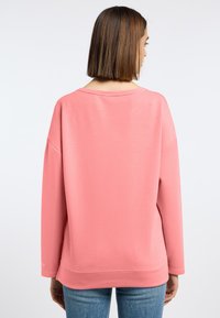 Roze sweatshirt met een relaxte pasvorm, wijde halslijn en verlaagde schouders, gecombineerd met lichtblauwe spijkerbroek. Eenvoudige textuur, minimalistisch ontwerp.