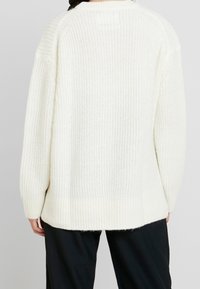 Maglione lavorato a maglia in bianco sporco, caratterizzato da un pattern testurizzato, maniche ampie e orlo a coste. La vista posteriore mette in evidenza la vestibilità rilassata e i dettagli delle cuciture delle spalle.