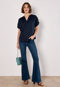 Navy short-sleeve blouse with a V-neck and gathered sleeve detail, paired with flared blue jeans and a light teal handbag.
