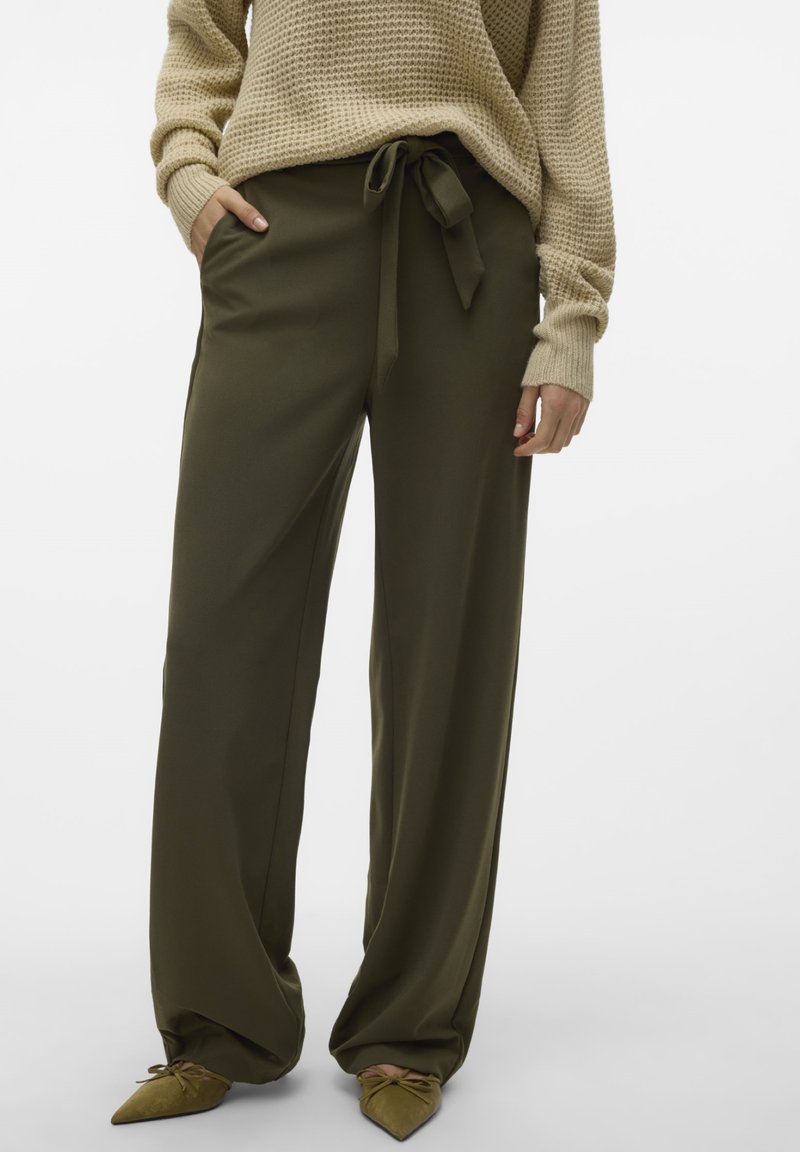 Pantalons larges vert olive avec une taille nouée, en tissu lisse. Portés avec un pull texturé beige et des chaussures vertes à bout pointu.