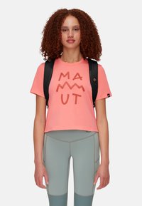 T-shirt corto corallo con grafica "MAMMUT" in corallo scuro. Indossato con leggings verde chiaro con cuciture e dettagli coordinati. Zaino nero.
