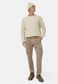 Beige langærmet skjorte, lyse corduroy cargo bukser og olivengrønne støvler. Modellen bærer en cremefarvet strikket hue. Simple design med funktionelle lommer.