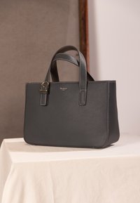 Sac fourre-tout en cuir texturé gris avec double poignée, ferrures dorées et branding minimaliste à l'avant. Forme rectangulaire aux bords lisses.