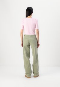 Haut rose à manches courtes avec épaules bouffantes, associé à un pantalon large vert clair. Texture lisse et coupe décontractée. Design simple.