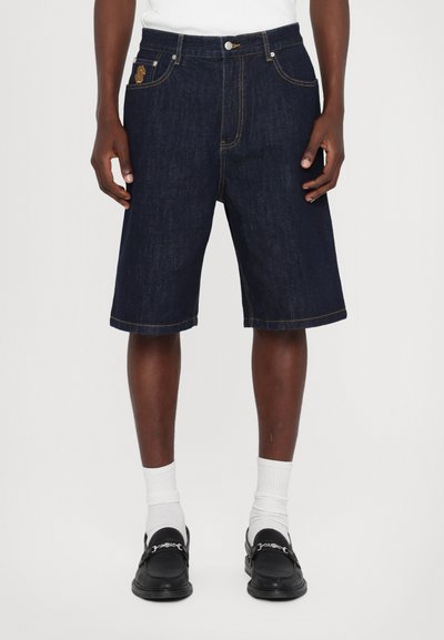 Shorts din denim de culoare bleu închis, cu o croială lejeră, margine răsucită și cusături contrastante de culoare portocalie. Două buzunare frontale cu detalii ale logo-ului.