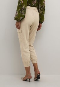 Béžové jogger kalhoty ze lněné směsi s elastickými manžetami a postranní kapsou na cargo, doplněné o zelený top s květinovým vzorem.