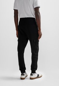 Svarta joggerbyxor i mjukt tyg, med sidofickor i cargo-stil och elastiska muddar. Kombinerade med vita sneakers.