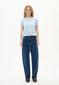 T-shirt azzurro chiaro a maniche corte, jeans in denim scuro a vita alta, cintura nera e ballerine con stampa leopardata, esposti su uno sfondo bianco.