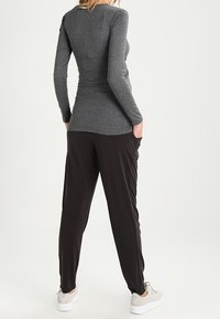 Graues langärmliges Oberteil mit einem taillierten Design und einer glatten Textur, kombiniert mit schwarzen lockeren Hosen und hellgrauen Turnschuhen.