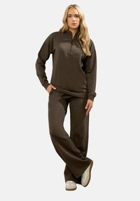 Pullover in pile marrone con colletto a zip e maniche lunghe, abbinato a pantaloni larghi coordinati. Tessuto testurizzato e design informale.