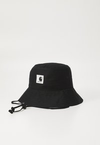 Black bucket hat made of cotton, featuring a white logo patch and a drawstring with adjustable toggle. Wide brim and textured fabric.