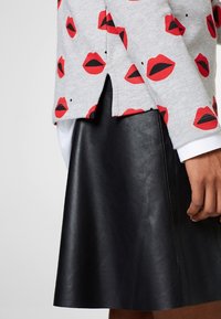 Grå sweatshirt med røde læbeaftryk, parret med en sort læderskirt. Skirten har en glat tekstur og en vidde form.