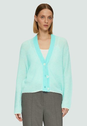Licht turquoise gebreid cardigan met een V-hals, vijf knopen en ribbelstructuur. Gedragen over een witte top, gecombineerd met grijze broeken.