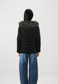 Svart boblejakke med imitasjonspelshette, quiltet tekstur og tilpasset silhuett; brukt med vide blå jeans.