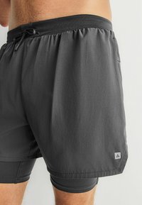 Grå badebukser af letvægtsstof med elastisk taljebånd og snøre, samt en logo-patch nær kanten.