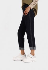 Pantalons en denim foncé avec coutures visibles, ourlets retroussés, associés à des baskets plateformes blanches avec un dessus texturé et un détail de logo.