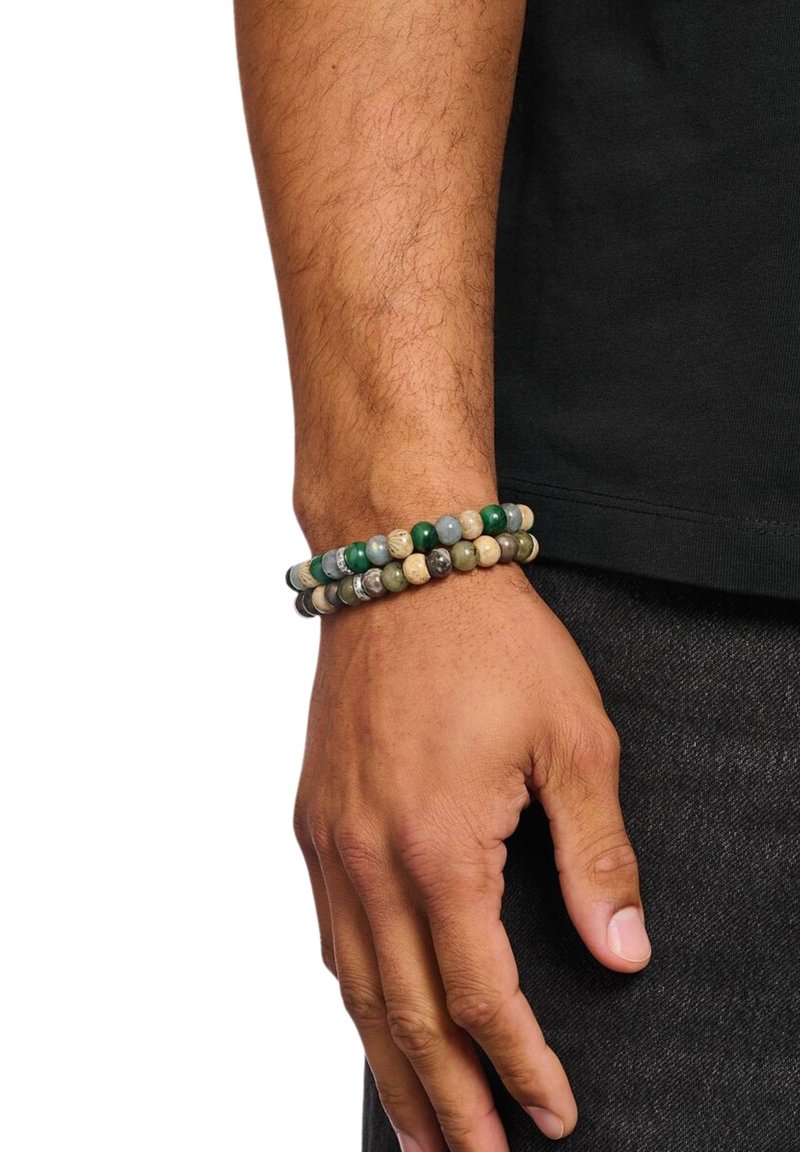 Multicolored bead bracelet featuring green, beige, and gray stones, elastic design, worn on a wrist, with a short-sleeve black shirt in view.