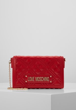 Pochette Love Moschino en cuir matelassé rouge avec bandoulière chaîne dorée et plaque logo métallique sur le devant, présentée sur un socle blanc.