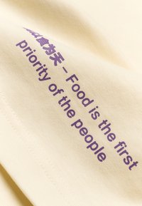 Υφασμα σε κρεμ απόχρωση με μωβ κείμενο που λέει «Το φαγητό είναι η πρώτη προτεραιότητα του λαού» στα Αγγλικά και στα Κινέζικα.